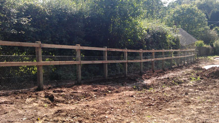 A long post and rail fence with chain link along a cleared boundary
